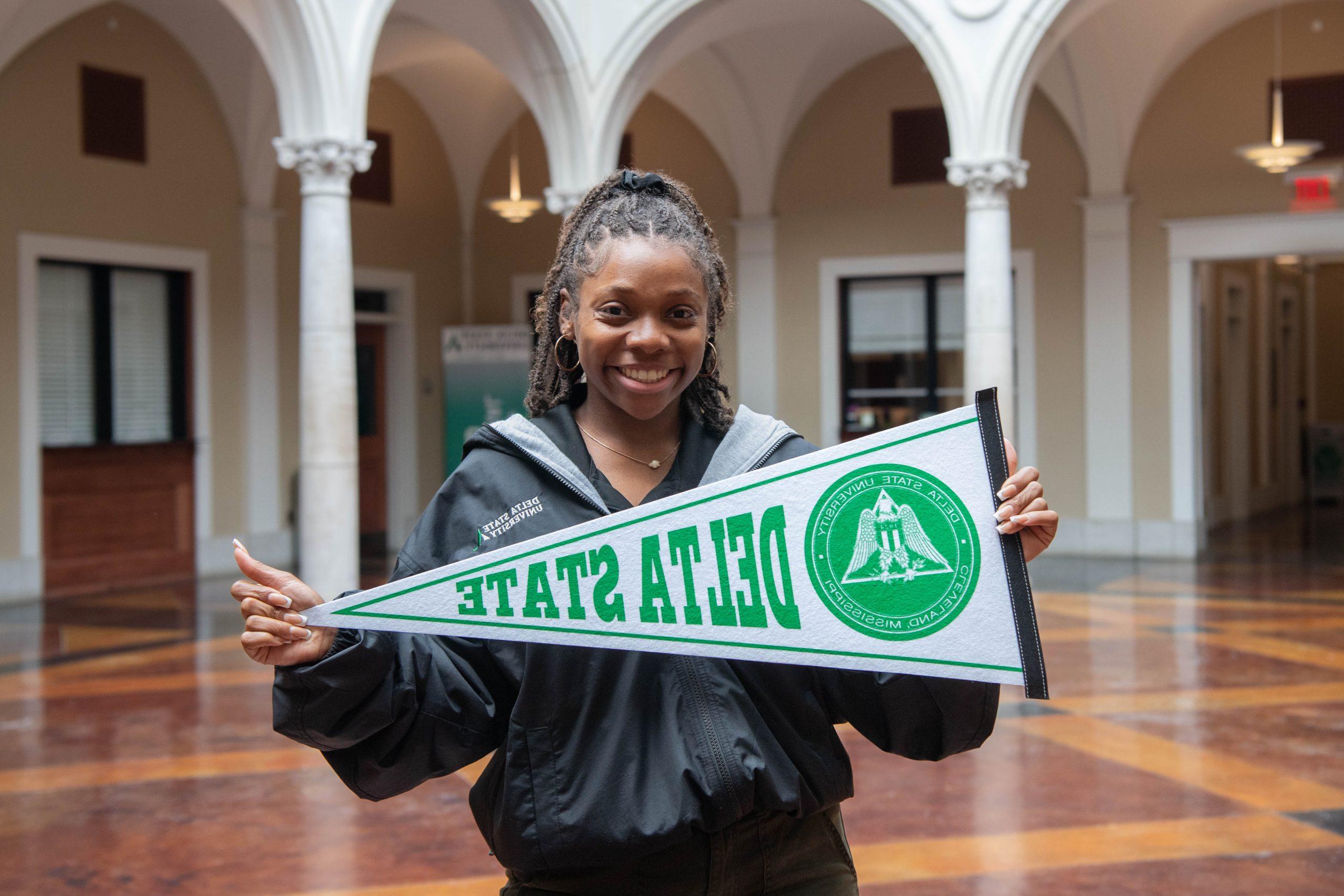 Admissions recruiter holding Delta State pennant in the administration building.